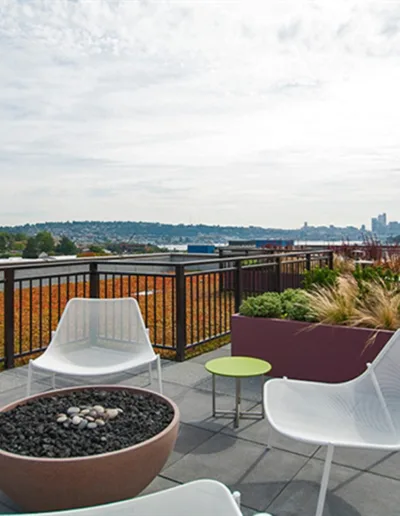 A rooftop patio with white chairs and a fire pit.